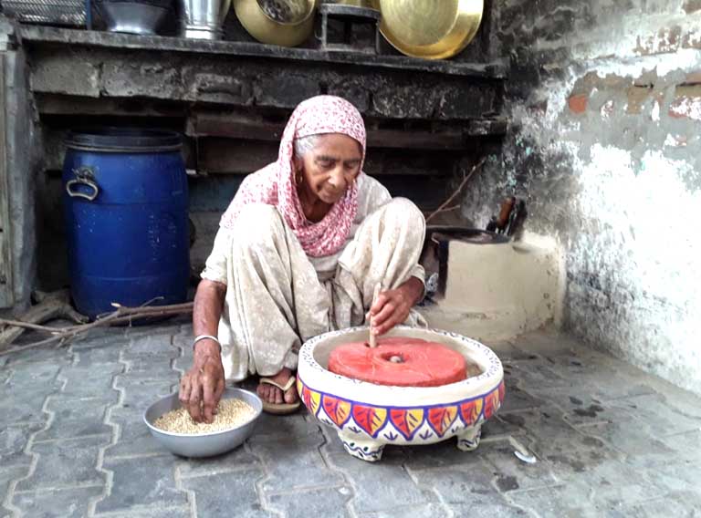 Grandmother at the hand mill by Gurleen Kaur